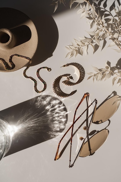 Esthetische luxe samenstelling met vrouwelijke sieraden en accessoires zonnebril oorbellen armband op witte achtergrond met glas in zonlicht schaduwen Elegante Boheemse plat lag bovenaanzicht mode-instelling