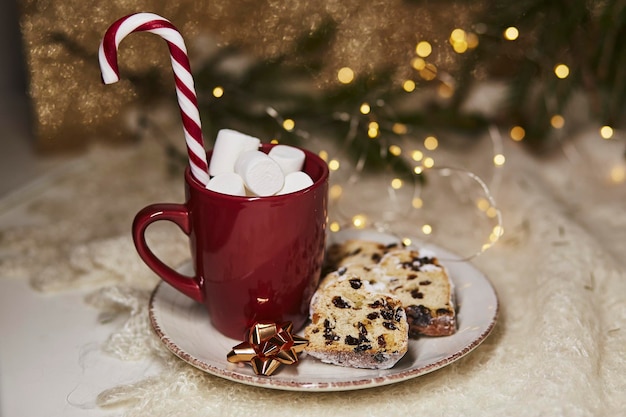 Esthetische warme drank rode kop met marshmallows en kerststol op keramische plaat traditionele feestdagen brood snoep kegelstok Feestelijke kerstachtergrond Kersttraditie eten