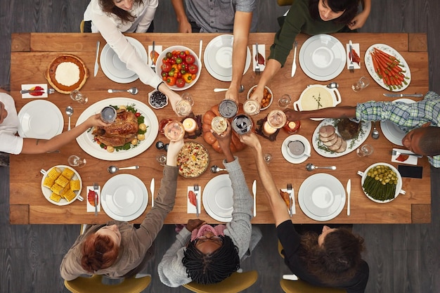 Eten bovenaanzicht en vrienden proosten aan een tafel om dankzegging te vieren op een feest of sociaal evenement samen Proost steun en gelukkige mensen met diversiteitsondersteuning en vertrouwen genieten van een dinermaaltijd