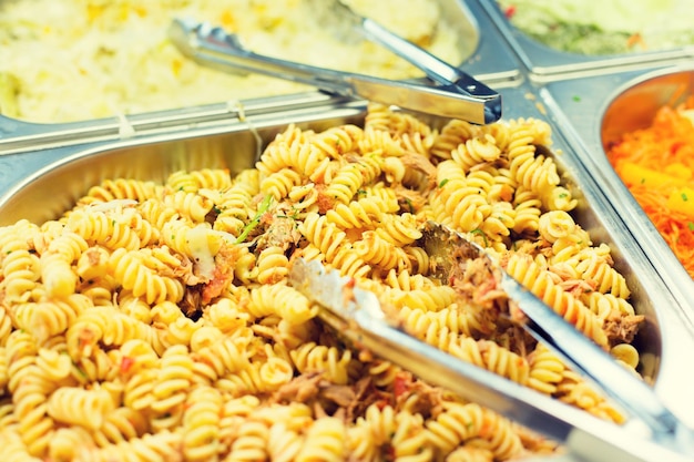 eten, catering, zelfbediening en eten concept - close-up van pasta en gerechten met een tang op metalen dienblad