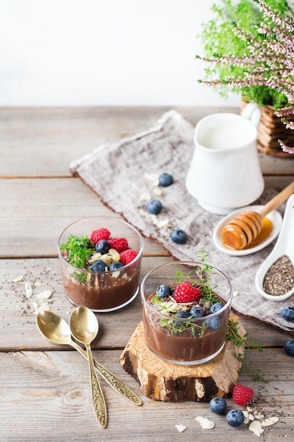 Eten en drinken gezond eten en dieet concept zelfgemaakte chocolade chia pudding met verse bessen en groene tijm voor het ontbijt op een gezellige houten keukentafel