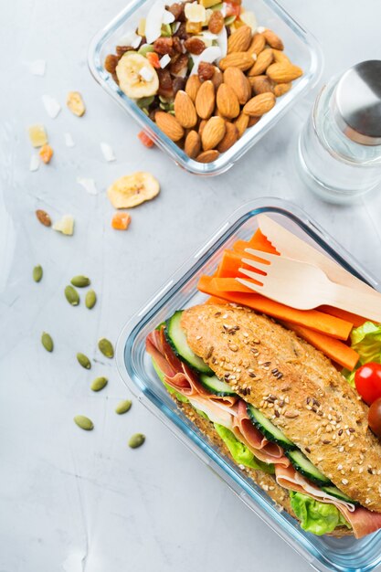 Eten en drinken, stilleven, dieet en voeding, gezond eten, afhaalconcept. lunchbox met boterham, fruit, groenten, notenmix en flesje water. bovenaanzicht plat lag achtergrond