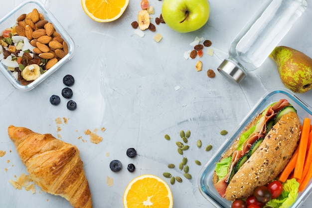 Eten en drinken, stilleven, dieet en voeding, gezond eten, afhaalconcept. Lunchbox met boterham, fruit, groenten, notenmix en flesje water. Bovenaanzicht plat lag, kopieer ruimte achtergrond