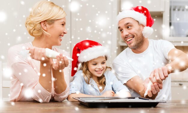 eten, familie, Kerstmis, geluk en mensen concept - lachende familie in santa helper hoeden die koekjes versieren met glazuur