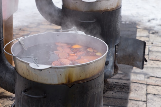 Eten koken op een houtkachel buiten op een verhard oppervlak met wintersneeuw, uitzicht vanuit een hoge hoek op de dampende pot en eten