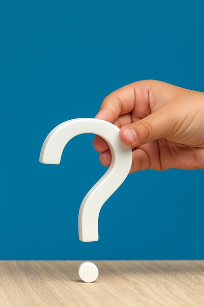 The eternal question the unknown or the search for an answer A hand holding a white question mark on a blue background Vertical photo with copy space High quality photo