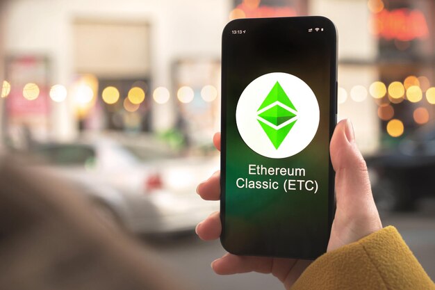 Ethereum classic etc cryptocurrency-symbool, logo. zakelijk en financieel concept. hand met smartphone, scherm met crypto icoon close-up