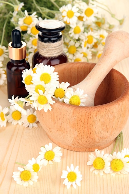 Etherische olie en kamille bloemen in vijzel op houten tafel