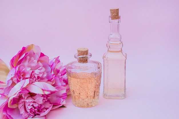 Etherische olieflessen en bloemen op roze achtergrond