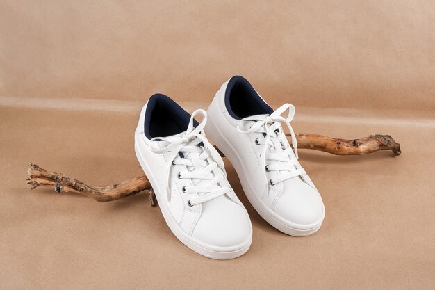 Ethical vegan shoes concept. pair of white sneakers on the wooden snag, neutral beige craft paper background.