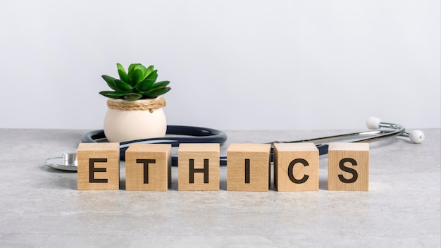 Ethics word written on wooden blocks and stethoscope on light gray background