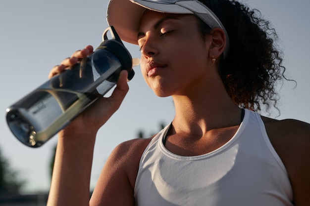 Ethnic tennis player drinking water