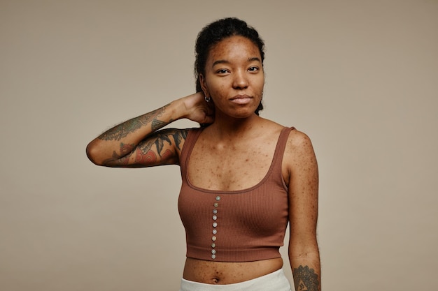 Этническая молодая женщина с татуировками смотрит в камеру на настоящую текстуру кожи