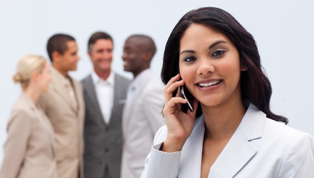 Etnische onderneemster op telefoon met haar team op de achtergrond