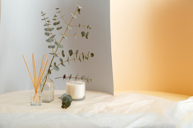 Eucalyptus branches bouquet in vase and Aromatic home perfume sticks, air freshener candle. Home Interior comfort element and aromatherapy with copy space on gray yellow and crumpled paper background.