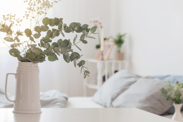 Eucalyptus en gypsophila in kruik in witte slaapkamer
