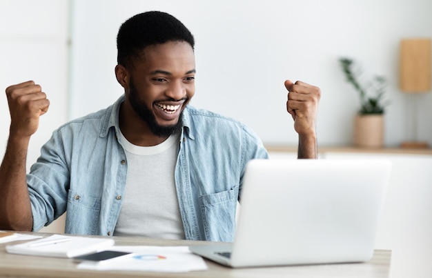 Euphoric black man celebrating business success with raised\
arms