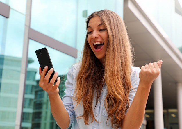 Euphoric business woman watching her smart phone and showing winner gesture outdoor