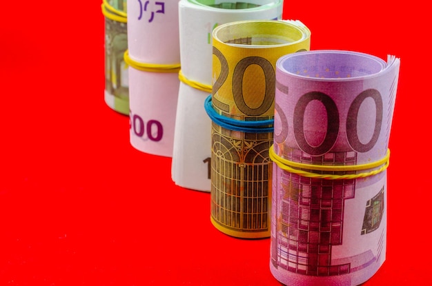 Euro banknotes of different denominations in rolls with elastic bands on a red background.