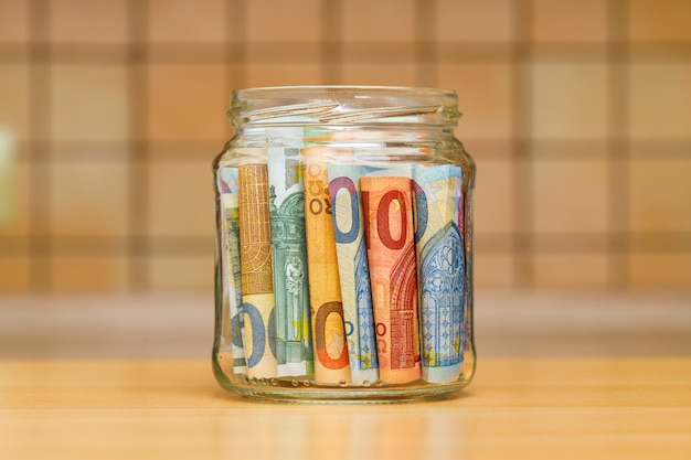 Euro banknotes in a glass jar close-up. the kitchen wall is blurred.