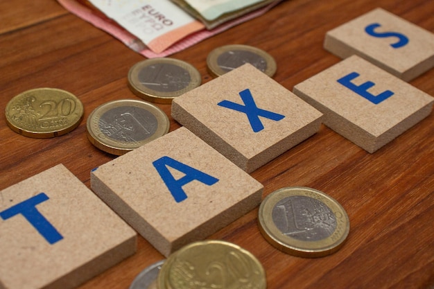 Euro banknotes and several coins on the wooden table written taxes