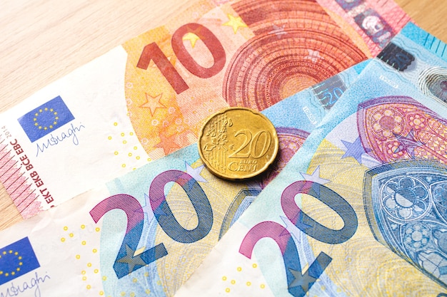 euro banknotes with a 20 cent coin on a piece of furniture