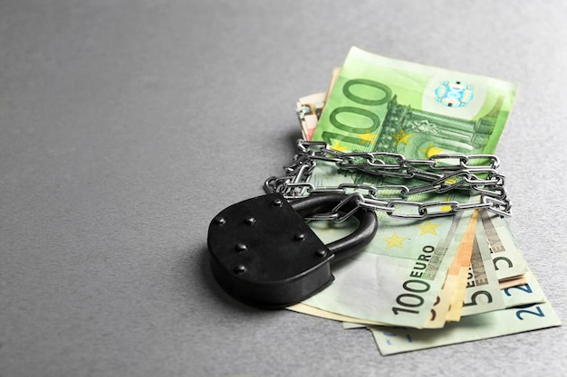 Euro banknotes with lock and chain on gray background