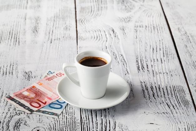 Euro bill and cup of coffee on wooden table. Payment, tip.