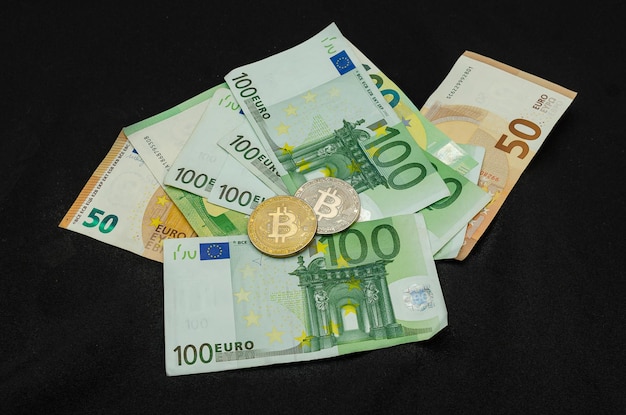 Банкноты евро и биткойн-монеты на черном фоне