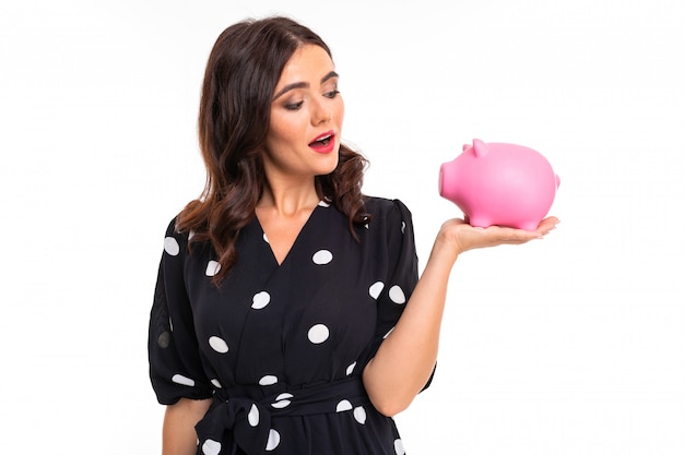 European attractive brunette holds a piggy bank in her hands on a white  with copyspace