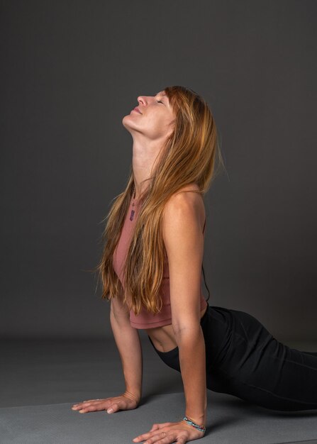 European beautiful girl with flowing blond hair is doing yoga Very bent back Grey background