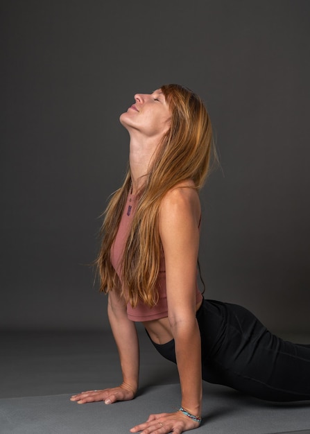 Photo european beautiful girl with flowing blond hair is doing yoga very bent back grey background