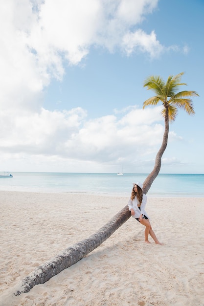 하얀 모래 해변의 코코넛 야자수 근처에 있는 유럽의 아름다운 행복한 검은 머리 소녀
