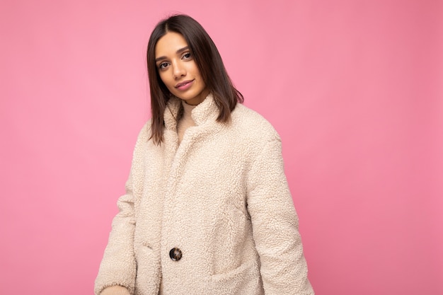 Foto bella giovane donna bruna europea che indossa un cappotto caldo beaige elegante isolato su sfondo rosa