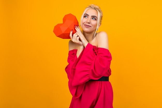 European blonde girl in love in red dress holds red paper heart