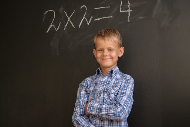 Европейский студент мальчик думает о решении математических задач, стоя у черной школьной доски