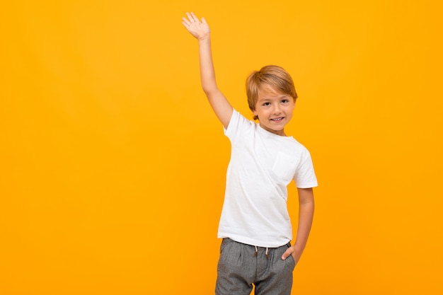 European boy in a white t-shirt with mockup with a raised hand on a yellow with copy space