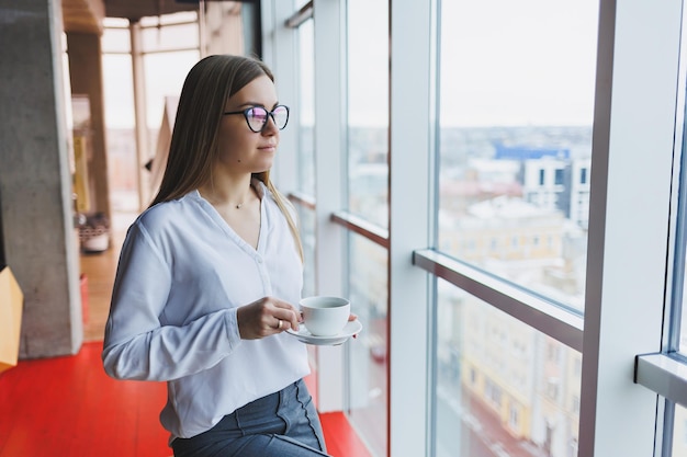 Donna d'affari europea che utilizza un computer portatile mentre lavora il concetto di una donna moderna di successo giovane bella donna sorridente con caffè seduto in un caffè interno ufficio aperto