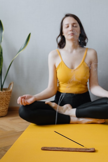 European caucasian woman does yoga and meditation in her home home calming yoga on a yellow mat