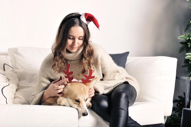 European caucasian young girl is sitting on the sofa with a corgi dog