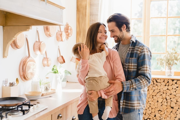 European caucasian young happy family parents with little small kid toddler spending time together at home kitchen embracing and hugging Parenthood concept