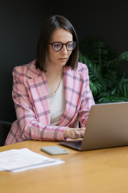 European confident business woman in a pink jacket and with a laptop in her office working