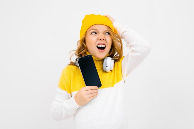 Photo european cute girl with big headphones and smartphone listens to music and grimaces over white background