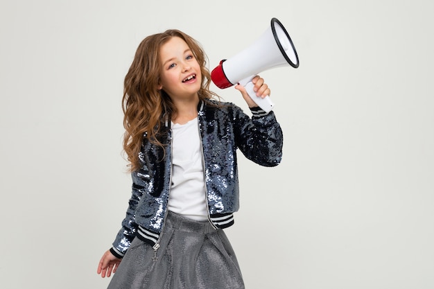 European cute teenager girl with a megaphone reports the news with a megaphone to her hands on a white studio background.