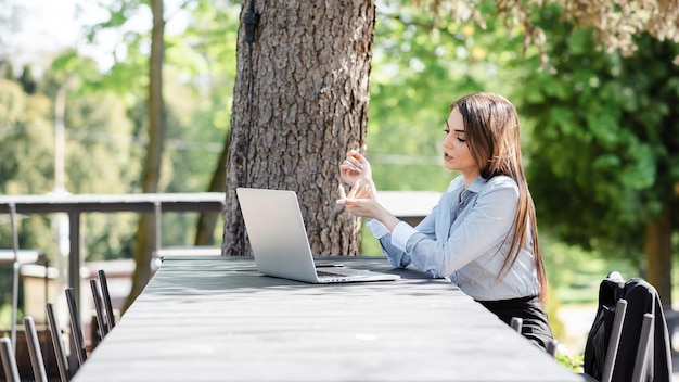 European dissatisfied businesswoman work on laptop computer outdoors Beautiful young girl sit at table in sunny park Modern woman lifestyle Concept of remote and freelance work