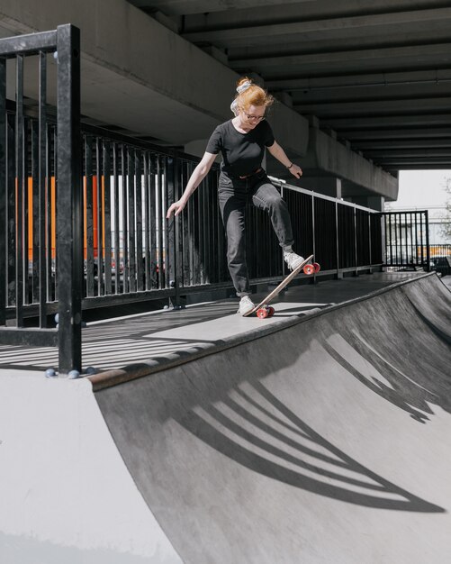 European female skater with red hair is riding a skateboard on a skate pad a woman in black clothes