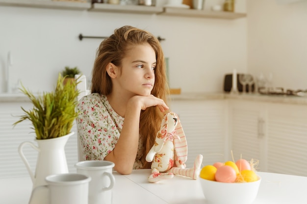 Photo european girl 10 years old in the kitchen at the table with easter eggs and a toy rabbit