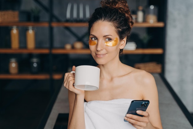 La ragazza europea beve caffè e manda messaggi sullo smartphone e si rilassa la routine serale per la cura del corpo