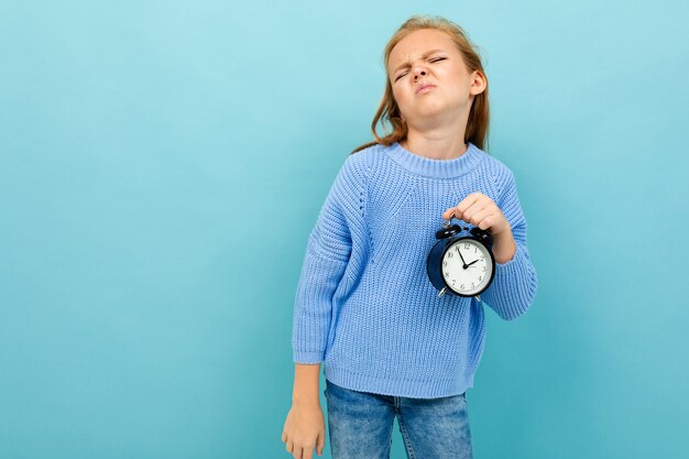 European girl holding an alarm clock on light blue