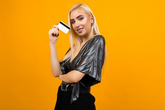 European girl holds a credit card with a mockup on a yellow studio surface